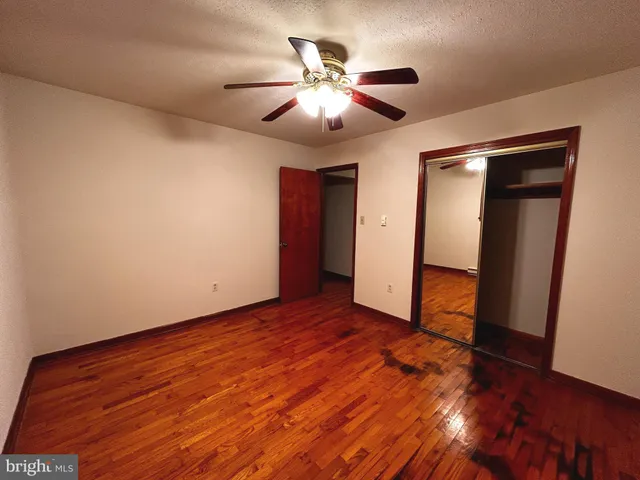 a view of an empty room with wooden floor and a ceiling fan