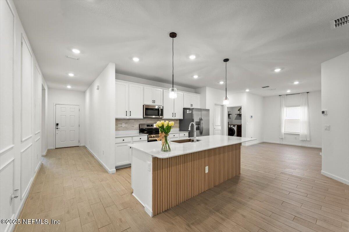 1598 Lachlan Circle Jacksonville, FL 32218 - Photo 14 of 38 a large white kitchen with kitchen island a sink a center island stainless steel appliances and a living room view