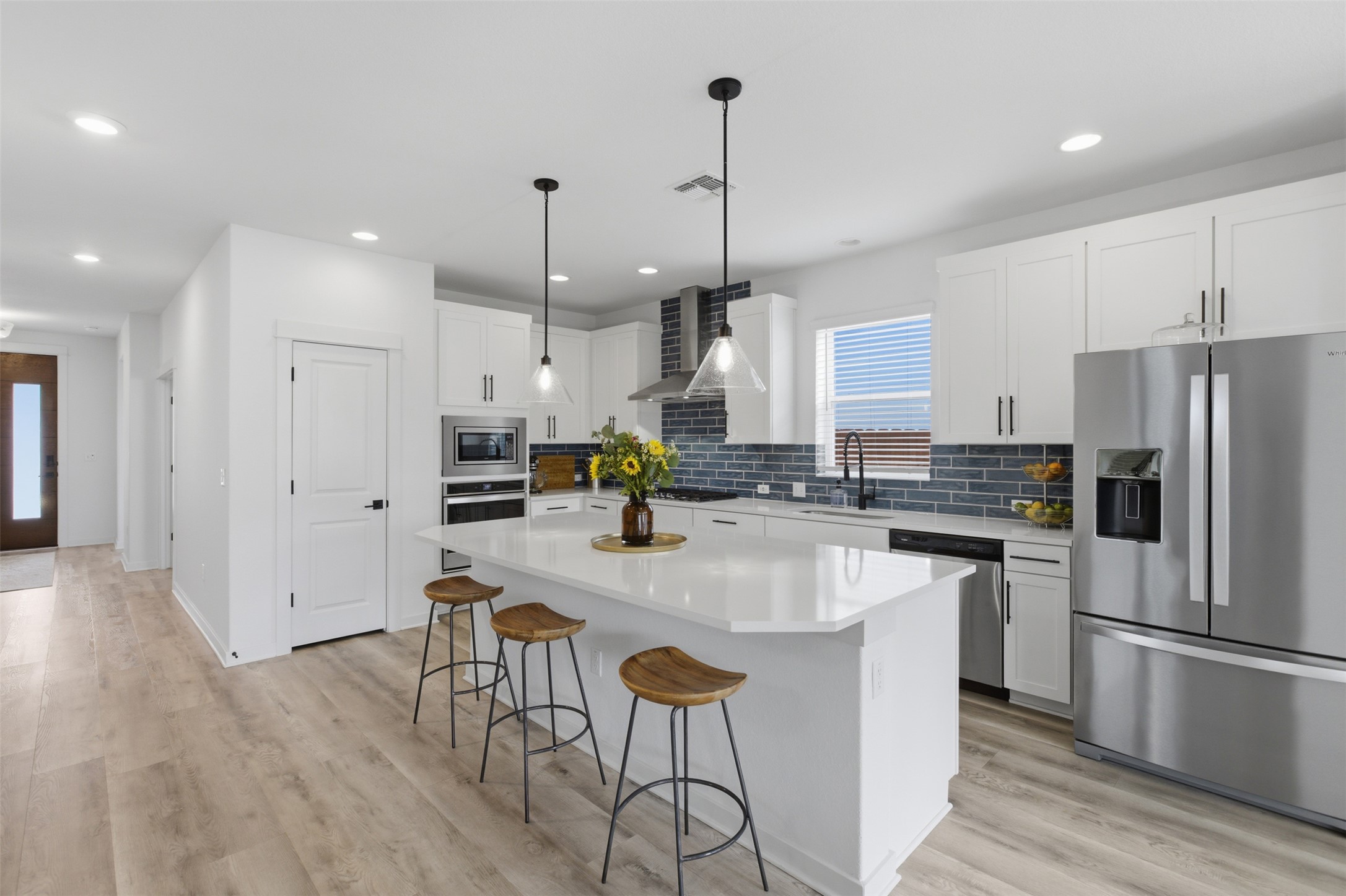 9001 Spire View Austin, TX 78744 - Photo 11 of 35 Modern kitchen featuring a large central island with seating, white shaker cabinetry, stainless steel appliances, and a dark blue tile backsplash