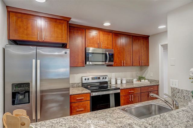 a kitchen with stainless steel appliances granite countertop a refrigerator a stove and a sink with wooden cabinets