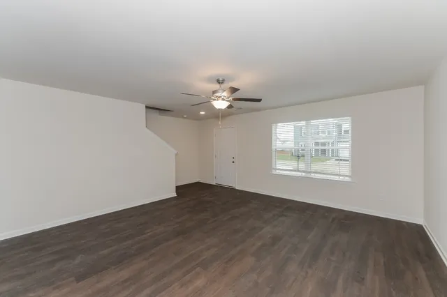 an empty room with wooden floor chandelier fan and windows