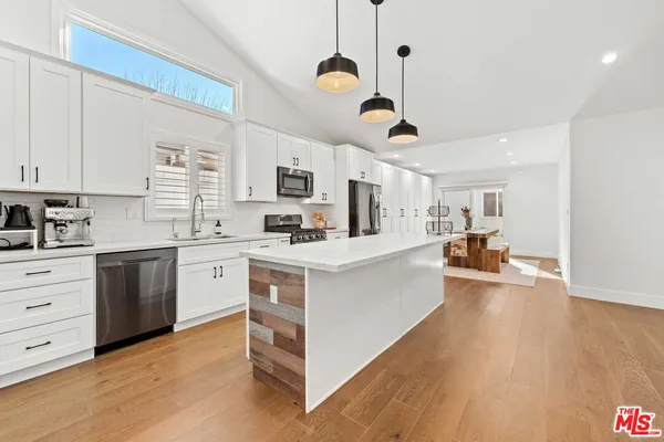 a large white kitchen with cabinets a sink a window and stainless steel appliances