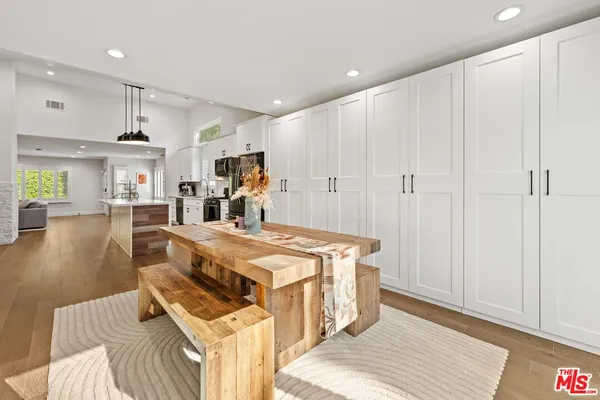 a very nice looking dining room with kitchen island a stove a sink a refrigerator and white cabinets with wooden floor