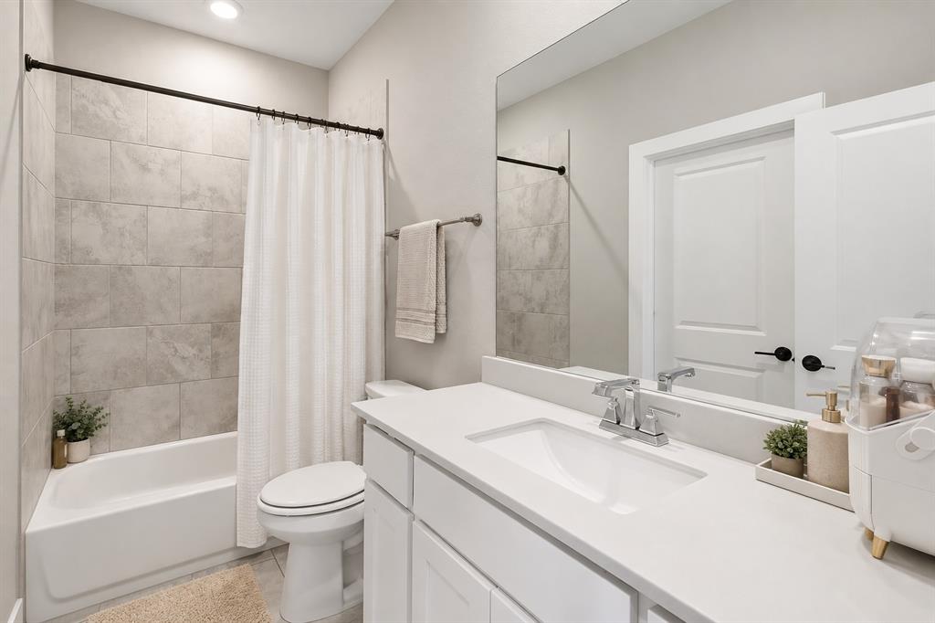 8408 Twistpine Road Frisco, TX 75035 - Photo 20 of 38 White vanity with an integrated sink and chrome faucet, large mirror, white bathtub with tiled surround, and recessed lighting