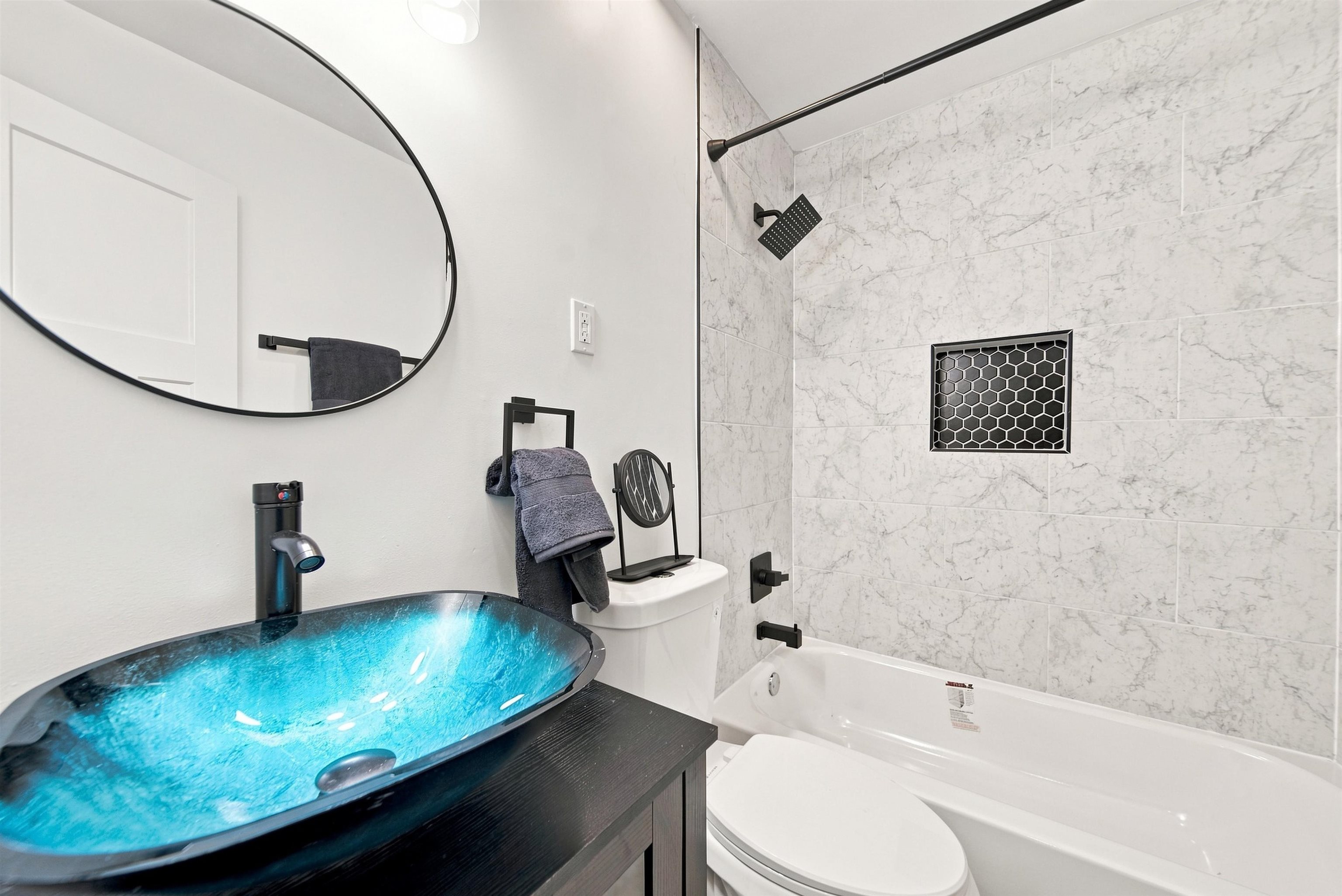 458 Gerald Road Memphis, TN 38122 - Photo 21 of 37 Blue glass vessel sink, dark-finish vanity, black fixtures, and a shower with white tile surround and black honeycomb niche