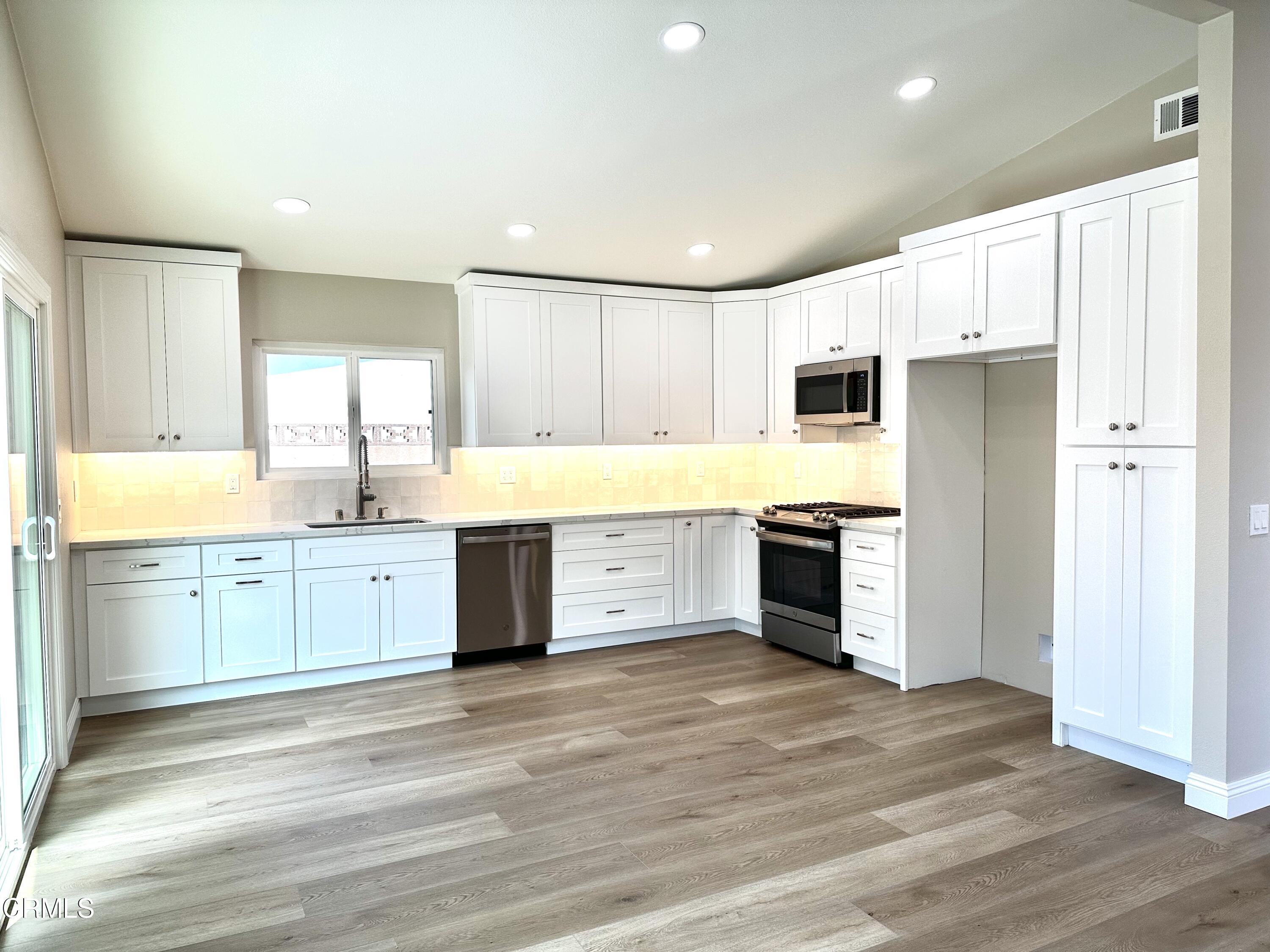 3031 Merced Place Oxnard, CA 93033 - Photo 6 of 26 a large kitchen with a stove a sink dishwasher a refrigerator and white cabinets with wooden floor