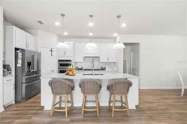 a kitchen with stainless steel appliances kitchen island granite countertop a dining table chairs refrigerator and sink