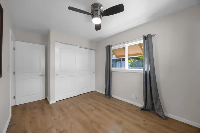 an empty room with wooden floor chandelier fan and windows