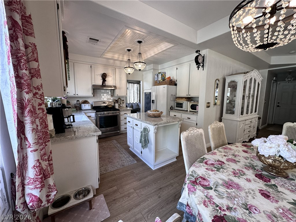 9724 Trail Rider Drive Las Vegas, NV 89117 - Photo 23 of 52 Kitchen featuring white cabinets, a tray ceiling, light stone countertops, stainless steel range oven, and suspended lighting