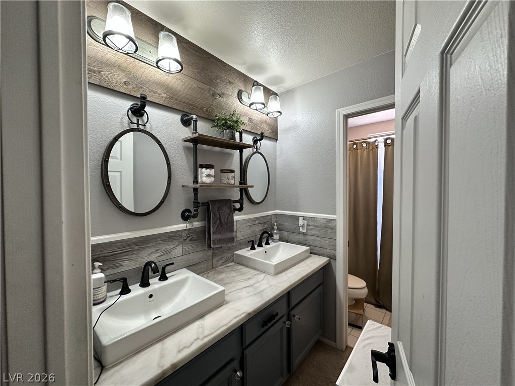 9724 Trail Rider Drive Las Vegas, NV 89117 - Photo 44 of 52 Bathroom featuring a textured wall, double vanity, a textured ceiling, curtained shower, and tile walls