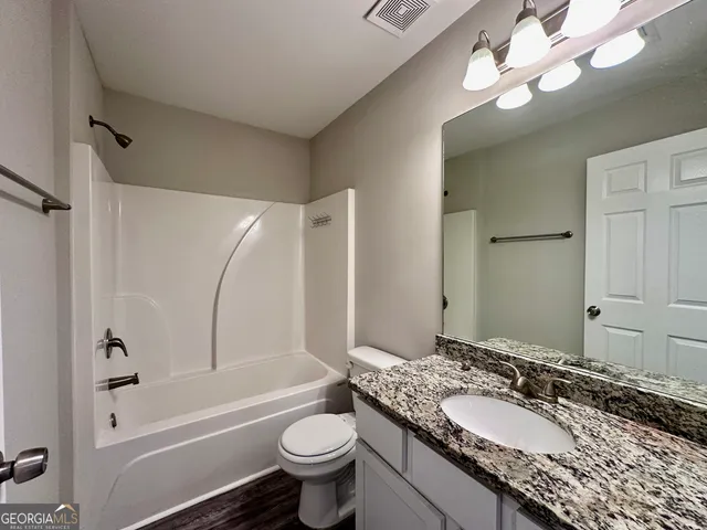 a bathroom with a granite countertop sink a toilet a mirror a bathtub and shower