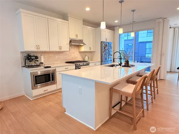 a kitchen with stainless steel appliances granite countertop a stove a sink a microwave a refrigerator and white cabinets with wooden floor