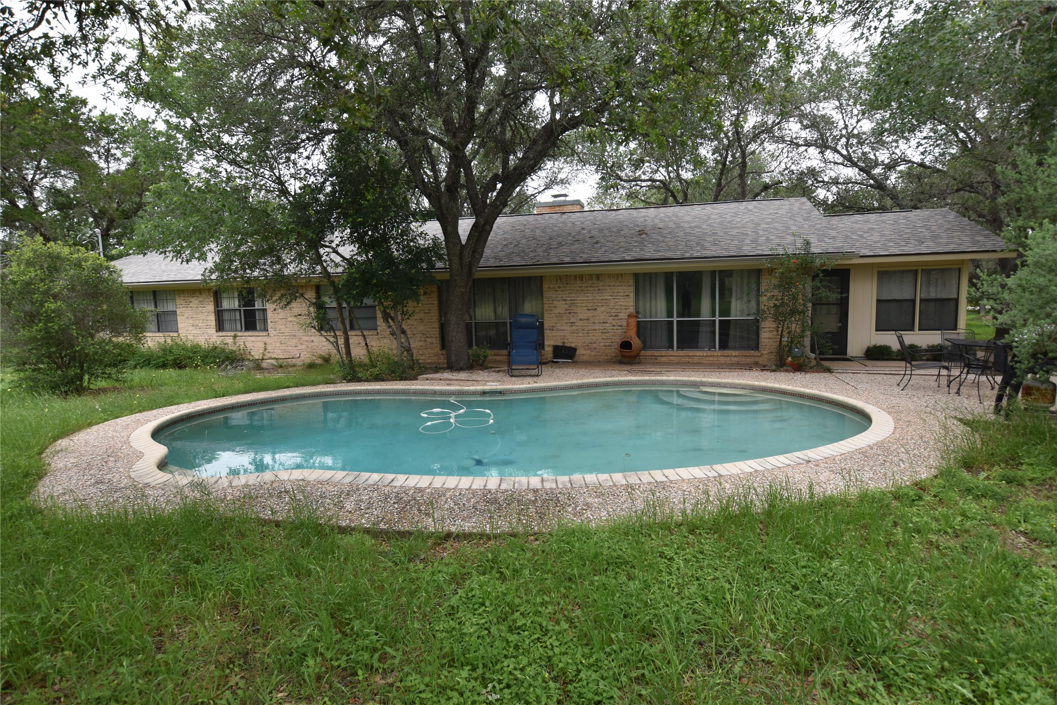 687 Fm 812 Road Red Rock, TX 78662 - Photo 39 of 40 Rear exterior featuring an oval swimming pool with integrated steps and a surrounding brick and aggregate coping