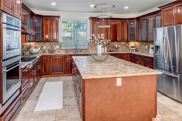a kitchen with stainless steel appliances granite countertop a refrigerator a stove and a sink with wooden cabinets