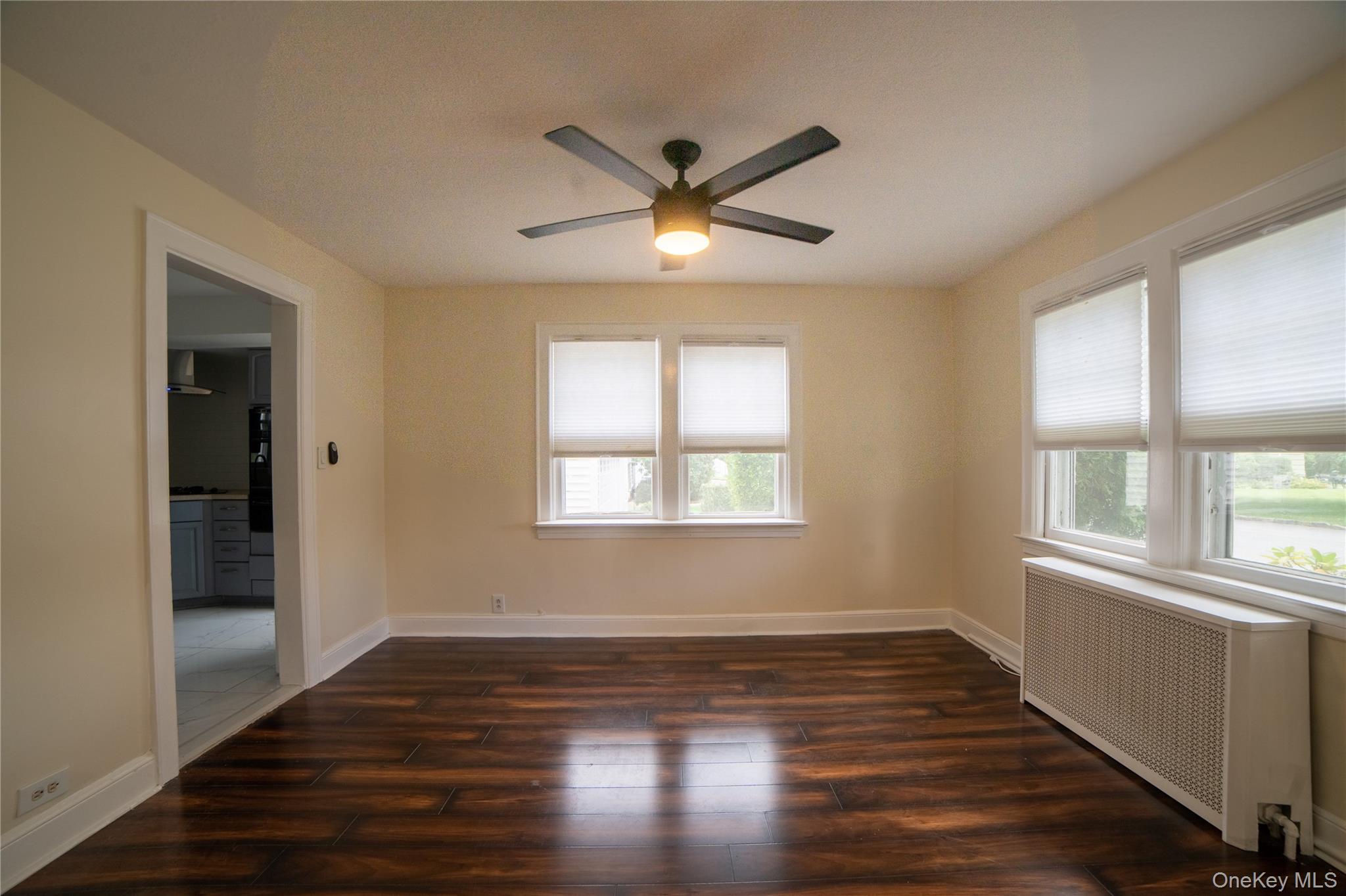 Dining room with ceiling fan and window blinds already in place and leading to the kitchen.