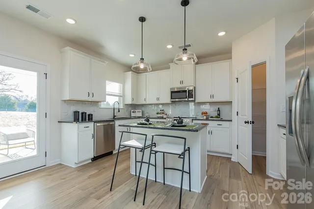 a kitchen with stainless steel appliances granite countertop a sink a stove a refrigerator and white cabinets with wooden floor