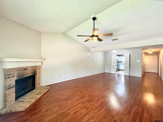 a view of an empty room with wooden floor fireplace and a window