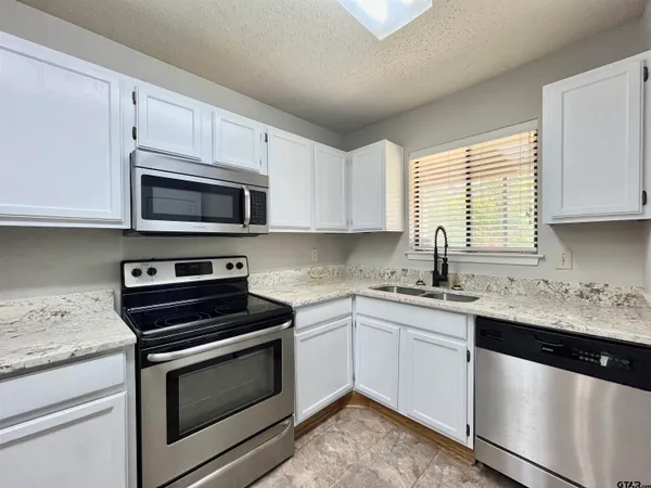 a kitchen with granite countertop white cabinets appliances and a window