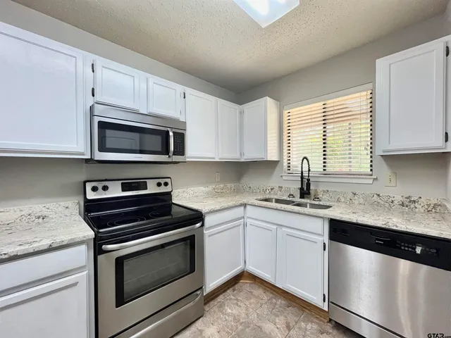 a kitchen with granite countertop white cabinets appliances and a window