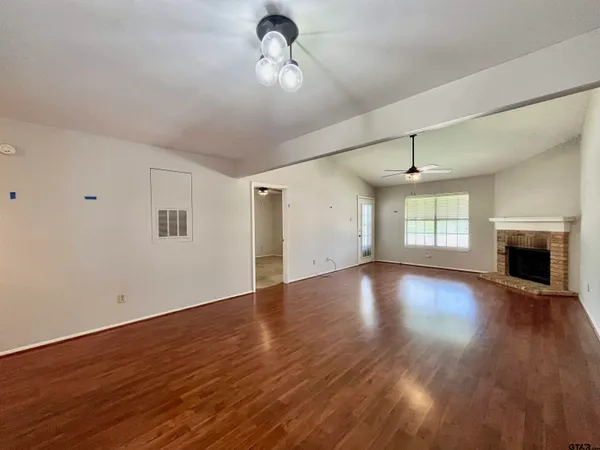 an empty room with wooden floor chandelier fan and windows