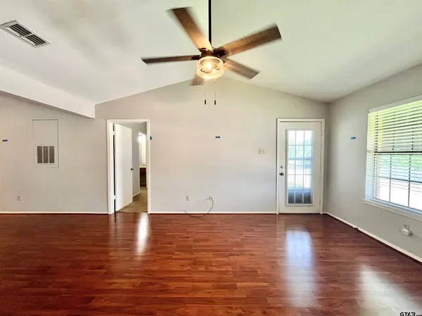 an empty room with wooden floor fan and windows