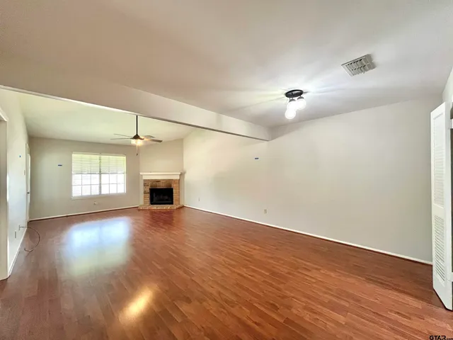 an empty room with wooden floor fireplace and windows