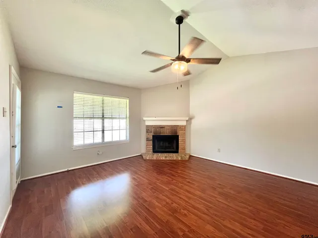 a view of an empty room with wooden floor fireplace and a window