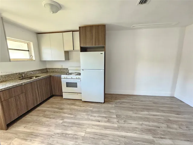 a kitchen with granite countertop a refrigerator a sink and white cabinets