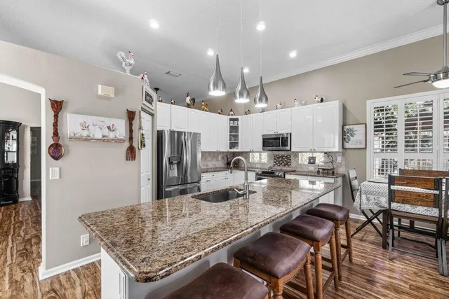 a kitchen with stainless steel appliances kitchen island granite countertop a refrigerator a stove top oven a sink dishwasher and white cabinets with wooden floor