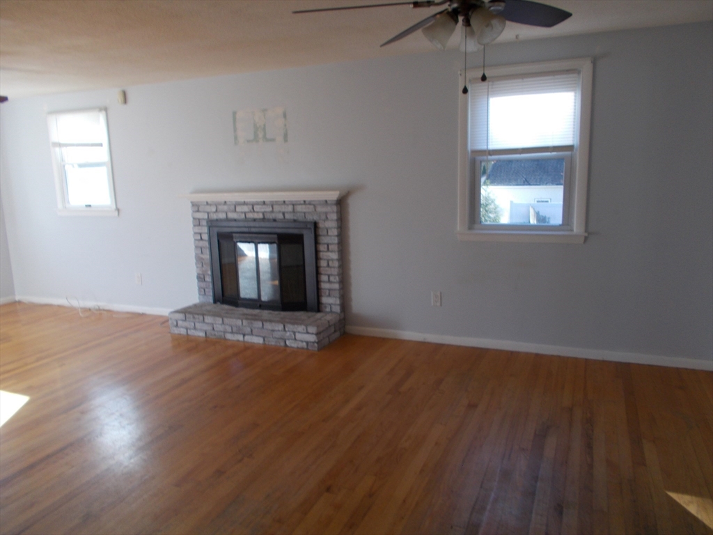 146 South Meadow Road Carver, MA 02330 - Photo 2 of 15 an empty room with wooden floor a fireplace and windows