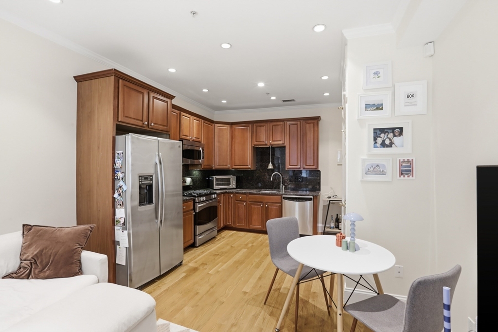 73 Myrtle Street, Unit 2 Boston, MA 02114 - Photo 7 of 13 a kitchen with stainless steel appliances kitchen island granite countertop a refrigerator a stove a sink a dining table and chairs with wooden floor