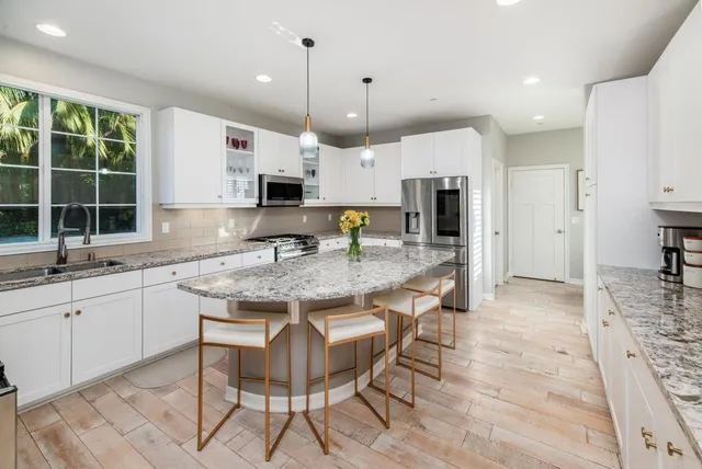 a kitchen with granite countertop kitchen island stainless steel appliances a sink and a refrigerator