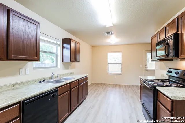 a kitchen with granite countertop wooden floors wooden cabinets and stainless steel appliances