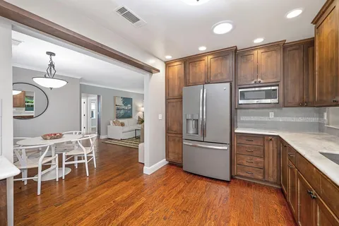a kitchen with stainless steel appliances granite countertop a refrigerator a microwave oven a sink dishwasher and white cabinets with wooden floor