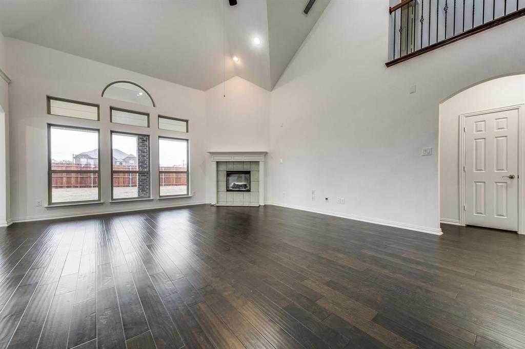 104 Sweetleaf Drive Red Oak, TX 75154 - Photo 10 of 36 Expansive living space featuring dark wood flooring, a fireplace with a light-colored mantel, and large windows with an arched top window