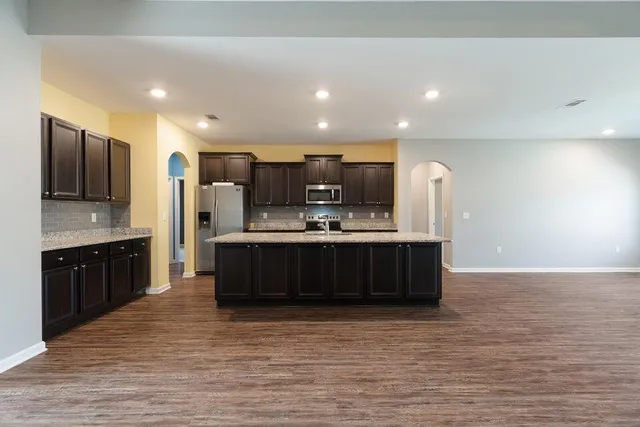 a kitchen with stainless steel appliances kitchen island granite countertop a large counter top and a wooden floors