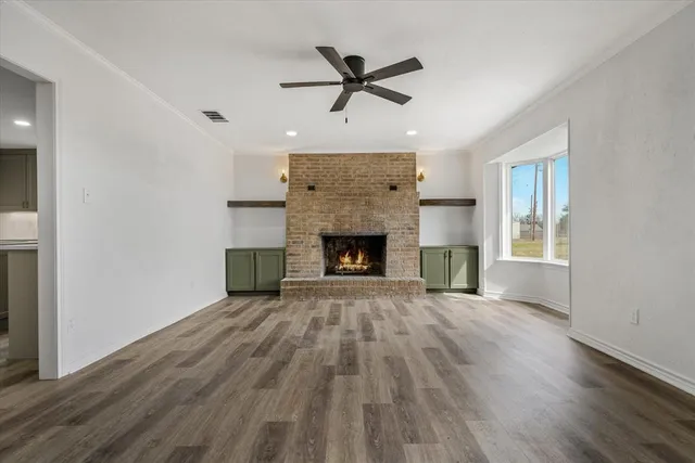 an empty room with wooden floor a fireplace a ceiling fan and a window