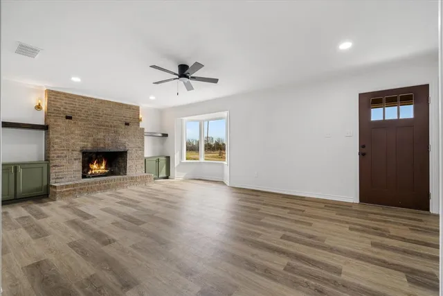 a view of an empty room with wooden floor fireplace and a window