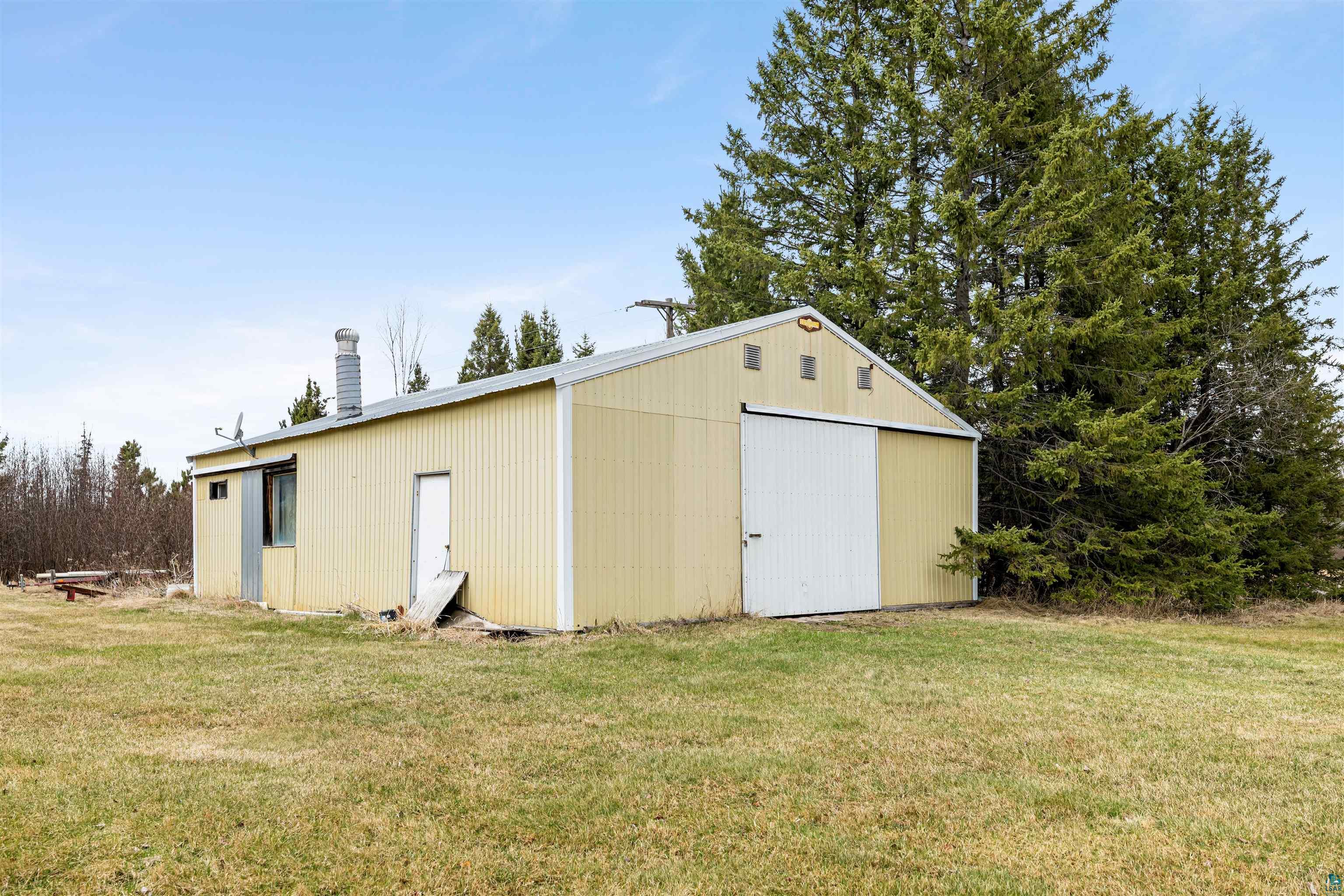 11574 Town Line Road Hibbing, MN 55746 - Photo 34 of 41 Light-colored corrugated metal outbuilding with a pitched roof, featuring a large white sliding barn door and an additional entry door