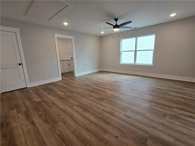a view of an empty room with wooden floor and a ceiling fan