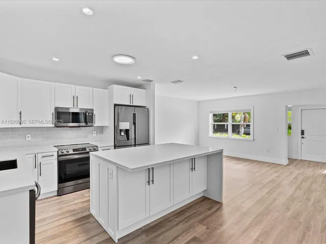 a kitchen with stainless steel appliances granite countertop a stove top oven a sink dishwasher and a refrigerator with wooden floor