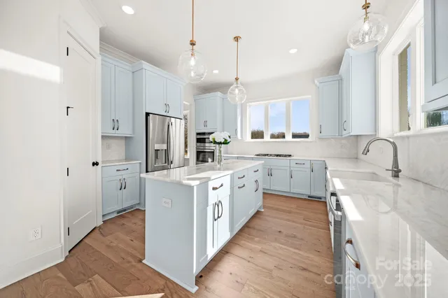 a white kitchen with stainless steel appliances granite countertop a sink a stove a refrigerator and island with wooden floor