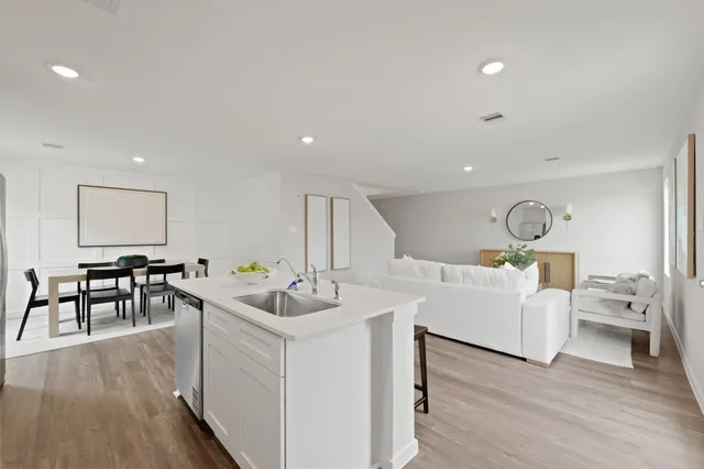 a living room with furniture a dining table wooden floor and white kitchen