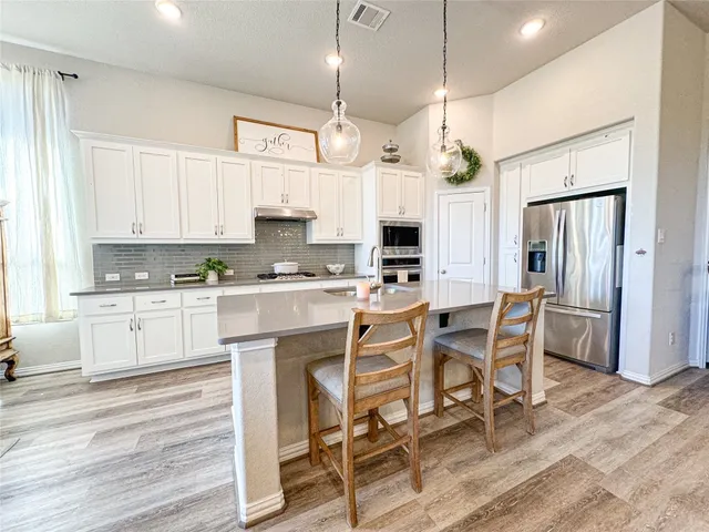 a kitchen with stainless steel appliances kitchen island granite countertop a table chairs refrigerator and microwave
