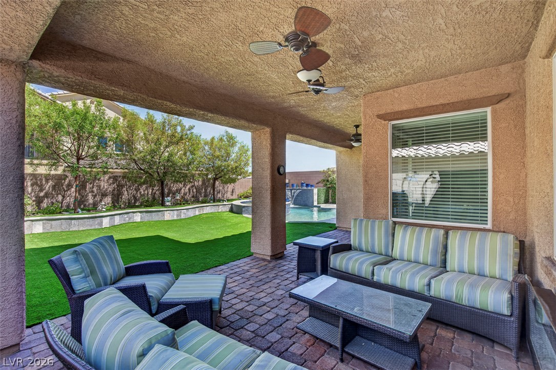 1824 Redland Ridge Street Henderson, NV 89002 - Photo 63 of 69 An inviting covered patio featuring paver flooring and ceiling fans overlooks a pristine lawn and pool area.