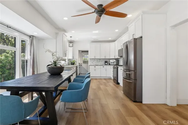a kitchen with stainless steel appliances kitchen island granite countertop a dining table chairs refrigerator and wooden floor