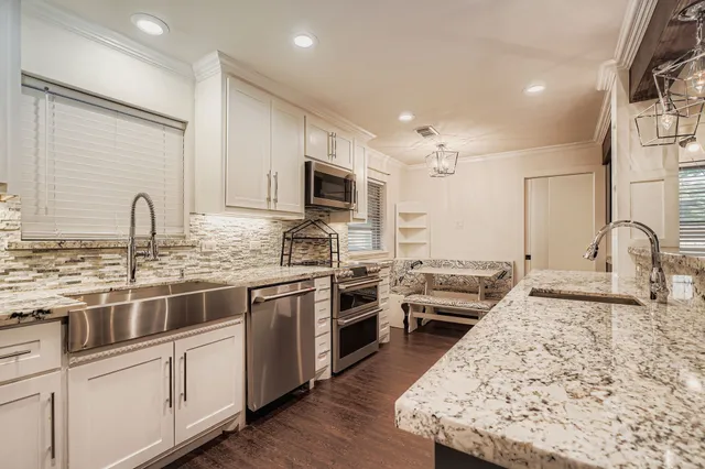 a kitchen with stainless steel appliances granite countertop a stove top oven a sink a refrigerator with white cabinets and wooden floor