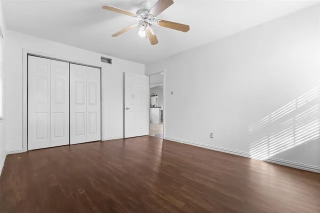 an empty room with wooden floor closet ceiling fan and windows