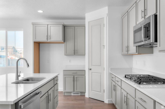 1024 South Tanner Road Santaquin, UT 84655 - Photo 13 of 20 Kitchen featuring gray cabinets, stainless steel appliances, wood finished floors, light stone countertops, and a textured ceiling