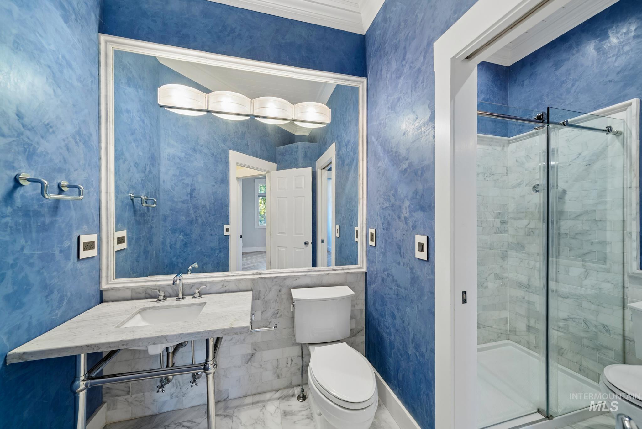2050 Artesian Road Eagle, ID 83616 - Photo 43 of 49 Bathroom featuring blue textured walls, a vanity with a white countertop and undermount sink, a large framed mirror, a four-light vanity fixture, and a glass-enclosed shower with tile surround